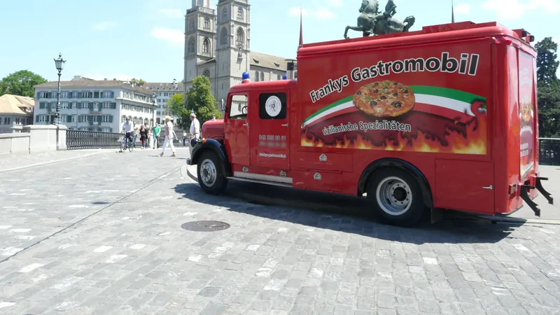 Das rote Feuerwehrauto von Frankys Gastromobil auf der Münsterbrücke in Zürich, dahinter das Grossmünster